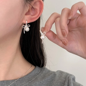 Detail view of silver bow-shaped earrings with round white pearls on ear and held in hand