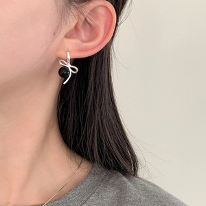 Detail showing elegant silver bow earrings with a black bead drop on a model's ear
