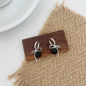 Detail of silver bow earrings with black agate beads on a rustic wooden display