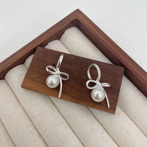 Detail of silver bow earrings with round white pearls on elegant wooden display