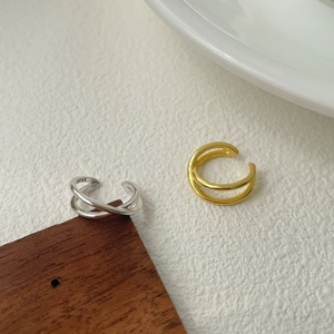 Close-up of gold and silver S925 cross ear cuffs on a minimalist white textured background