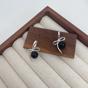 Detailed view of S925 silver bow earrings with black agate beads on a wood display