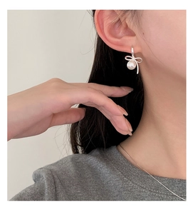 Close-up of silver bow pearl earrings worn on ear showing elegant jewelry details