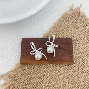 Detail of silver bow earrings with round white pearls on a rustic wooden stand
