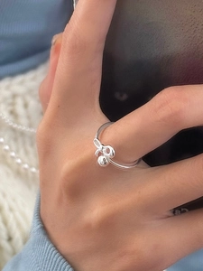 Vista macro di un anello a fiocco in argento S925 con pendente a sfera su mano femminile