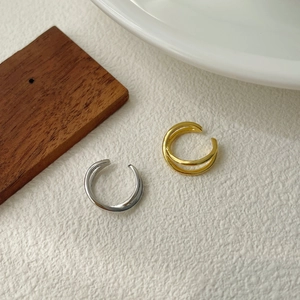 Macro detail of gold and silver X-shaped double-layer metal ear cuffs on textured surface