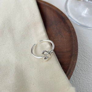 Dettaglio dell'anello con fiocco in argento e perla pendente su legno e lino rustico