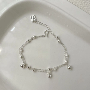 Détail d'un bracelet double couche en argent S925 avec pendentifs en cœur et perles