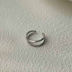Detailed close-up of a minimalist silver double-layer X-shaped ear cuff on beige fabric