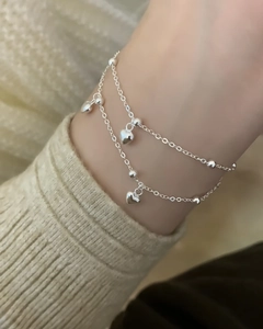 Gros plan d'un bracelet double couche en argent avec cœurs et perles sur le poignet