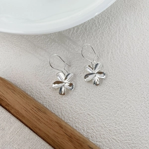 Close-up of silver S925 flower drop earrings with minimalist five-petal design on white stone