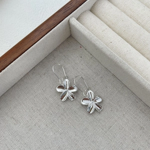 Detailed view of polished silver 5-petal flower earrings in a beige gift box
