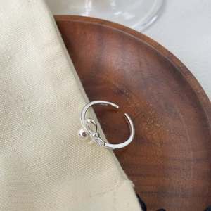 Dettaglio dell'anello a fiocco in argento S925 con finitura lucida su sfondo minimalista