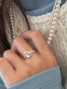 Dettaglio dell'anello in argento S925 con fiocco e ciondolo su modella con perle