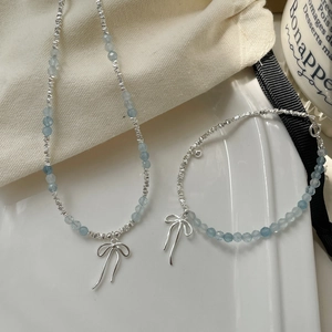 S925 sterling silver bracelet with blue aquamarine beads and a bow pendant on a plate