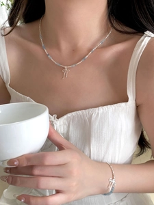 Detail of silver bow pendant necklace and blue beaded bracelet set on model