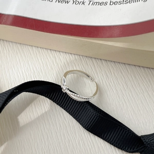 Detailed close-up of a silver twist-knot open ring on a black textured ribbon backdrop