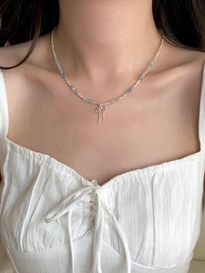 Detail of a blue aquamarine beaded necklace with a silver bow pendant on a model