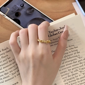 Macro detail of a minimalist gold twisted rope ring worn by hand on a book background