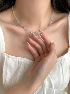 Close-up of a silver bow pendant on a light blue beaded necklace worn by a model