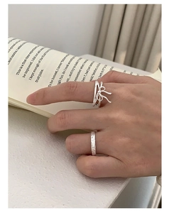 Detail of S925 silver ribbon bow ring and hammered band worn on finger over book