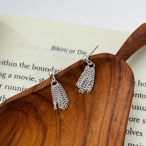 Macro detail of S925 sterling silver tassel drop earrings on a rustic wooden spoon