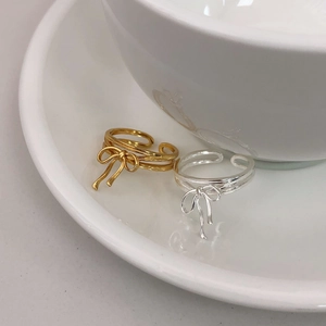 Close-up of gold and silver S925 sterling silver ribbon bow rings on ceramic dish