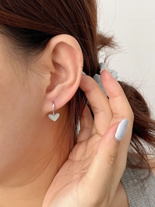 Close-up showing the fit of silver S925 heart-shaped hoop earrings on a model's ear