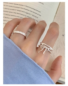 Detail of S925 silver ribbon bow ring and hammered band on model hand with book