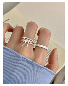 Detail of silver bow and hammered rings on hand with cozy blue knitted sleeve background