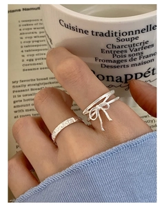 Detail of S925 silver bow ring and hammered texture band worn on finger with soft lighting