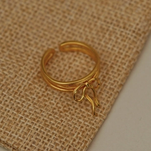 Detail view of a vintage gold ribbon bow ring on a textured fabric background