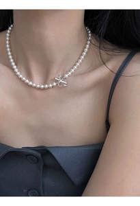 Elegant round faux pearl necklace with silver bow pendant on a model's neck