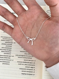 Detailansicht einer eleganten S925 Silber Schleife Halskette gehalten vor einer Buchseite