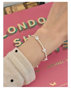 Close-up of S925 silver bracelet with bow charms and textured beads on woman's wrist