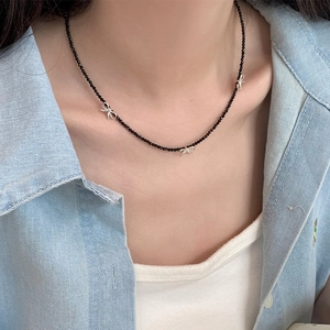 Détail d'un collier en perles noires avec des nœuds argentés porté sur du denim