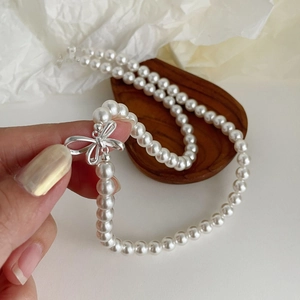 Close-up of pearl necklace featuring a detailed silver bow clasp on a dark wooden stand