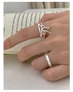 Macro detail of S925 silver bow ribbon ring and textured wide band on a book