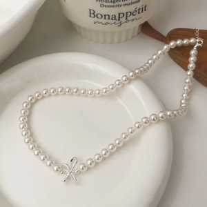 Detail shot of a S925 silver bow pendant and round white pearl necklace with lobster clasp