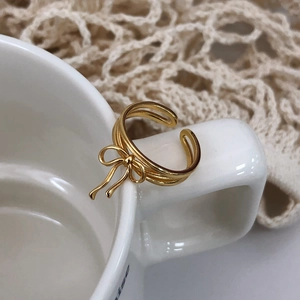Detailed view of a gold ribbon bow ring displayed on a white ceramic cup edge