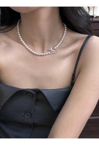 Detail of round faux pearl necklace with silver bow pendant shown on collarbone