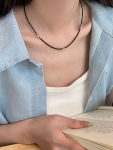Détail d'un collier de perles noires fines avec pendentifs nœuds argentés sur le cou