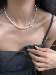Detail of elegant white round pearl necklace with silver bow pendant on model