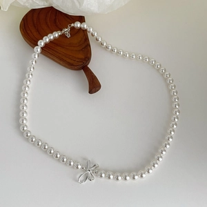 Detail of round faux pearl necklace featuring a silver metallic 3D bow pendant decoration