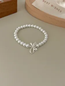 Detail of elegant S925 silver bow and round white pearl bracelet on a silk gift bag