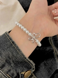 Detail of s925 silver bow charm with white pearls worn on wrist for a sweet aesthetic