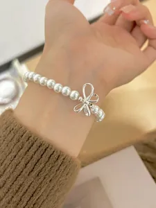 Detail of elegant white pearl bracelet featuring a silver 3D bow charm on a hand