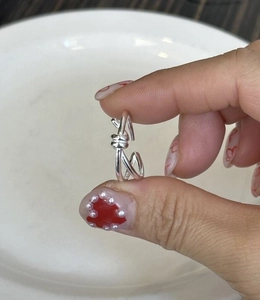 Detail view of S925 silver knot ring with elegant twisted line design held over a plate