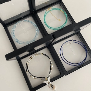 Detail of beaded gemstone necklaces with butterfly charm in black floating display boxes