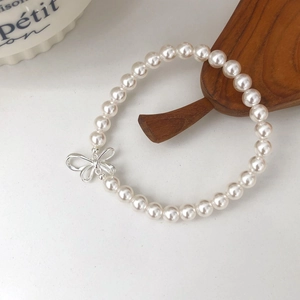 Detailed close-up of a white round pearl bracelet with a silver bow charm on a white surface